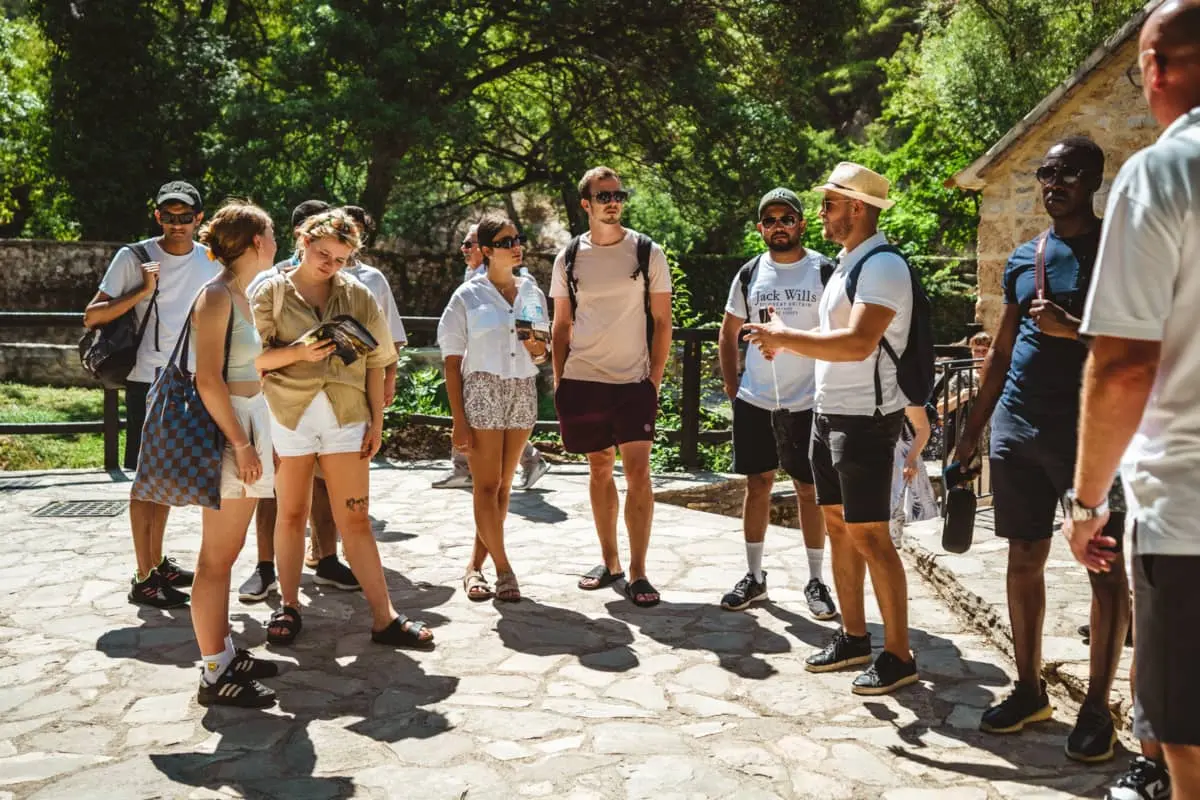 A group of people standing in a semi-circle on one of the trails in Krka National Park, engaged in conversation with a Tour Guide, learning about the park's attractions.